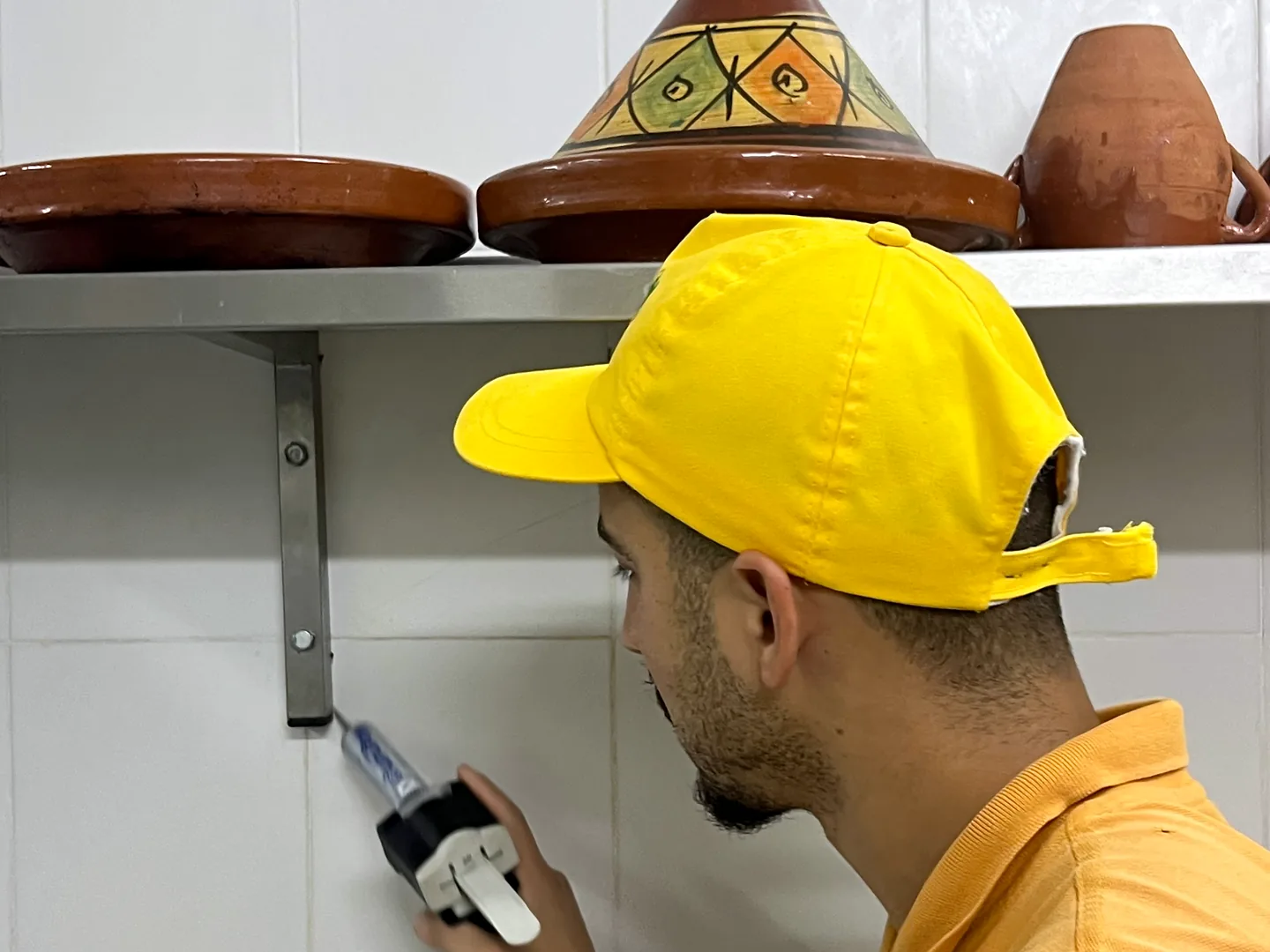 Un technicien Deratizon applique un gel insecticide sous une étagère de cuisine, près des tajines.